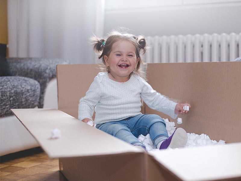 smiling toddler sitting in moving box with packing peanuts